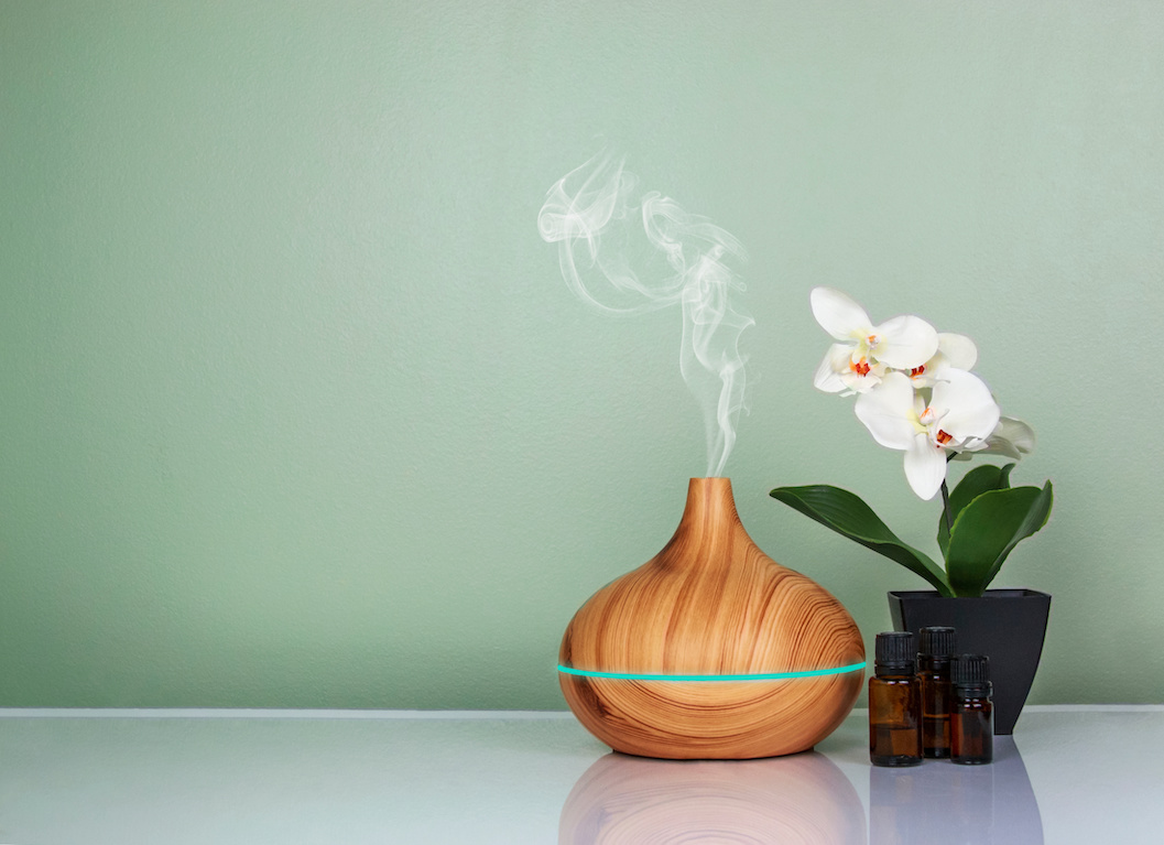 Electric Essential oils Aroma diffuser, oil bottles and flowers on light green surface with reflection. The calming effects of aromatherapy in manicure and pedicure routines.